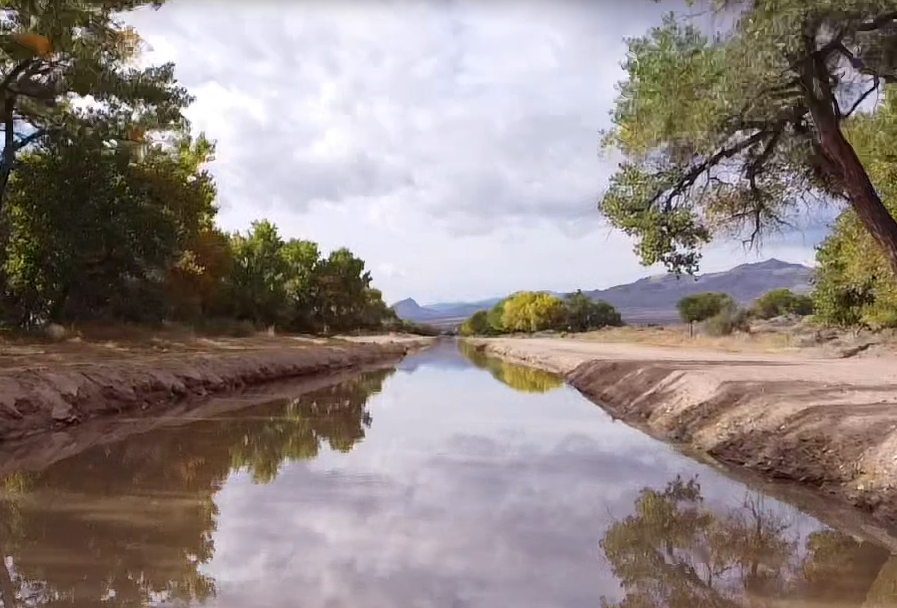 MRGCD canal near Socorro, NM, reflecting cloudy skies, lined by cottonwoods with mountains beyond